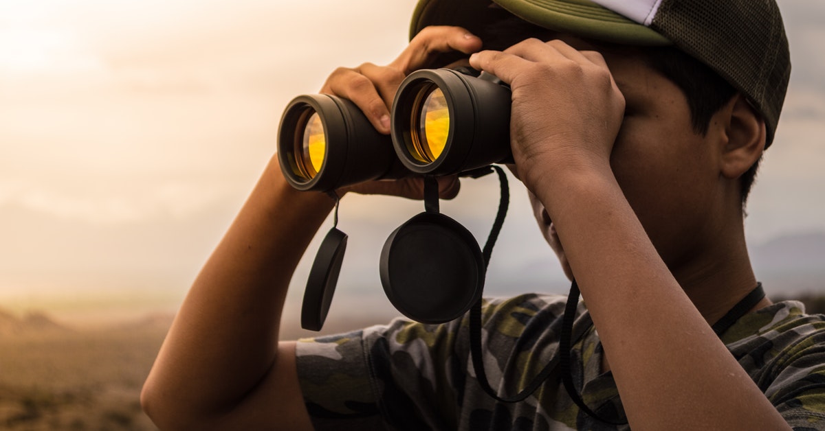 man looking in binoculars during sunset